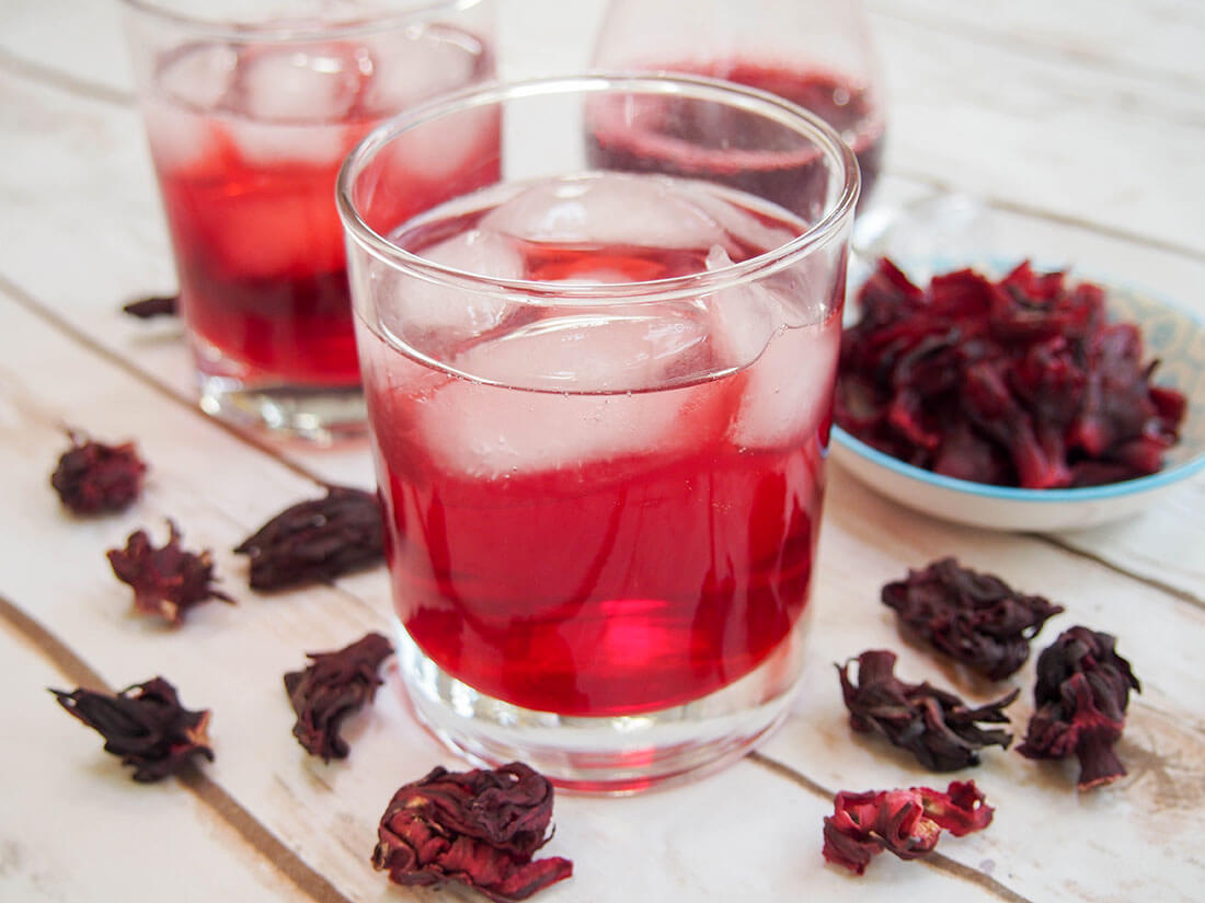 Agua de jamaica - hibiscus tea glass with flowers and syrup behind