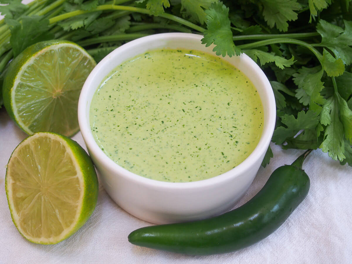 dish of aji verde Peruvian green sauce with cut lime to side and chili in front