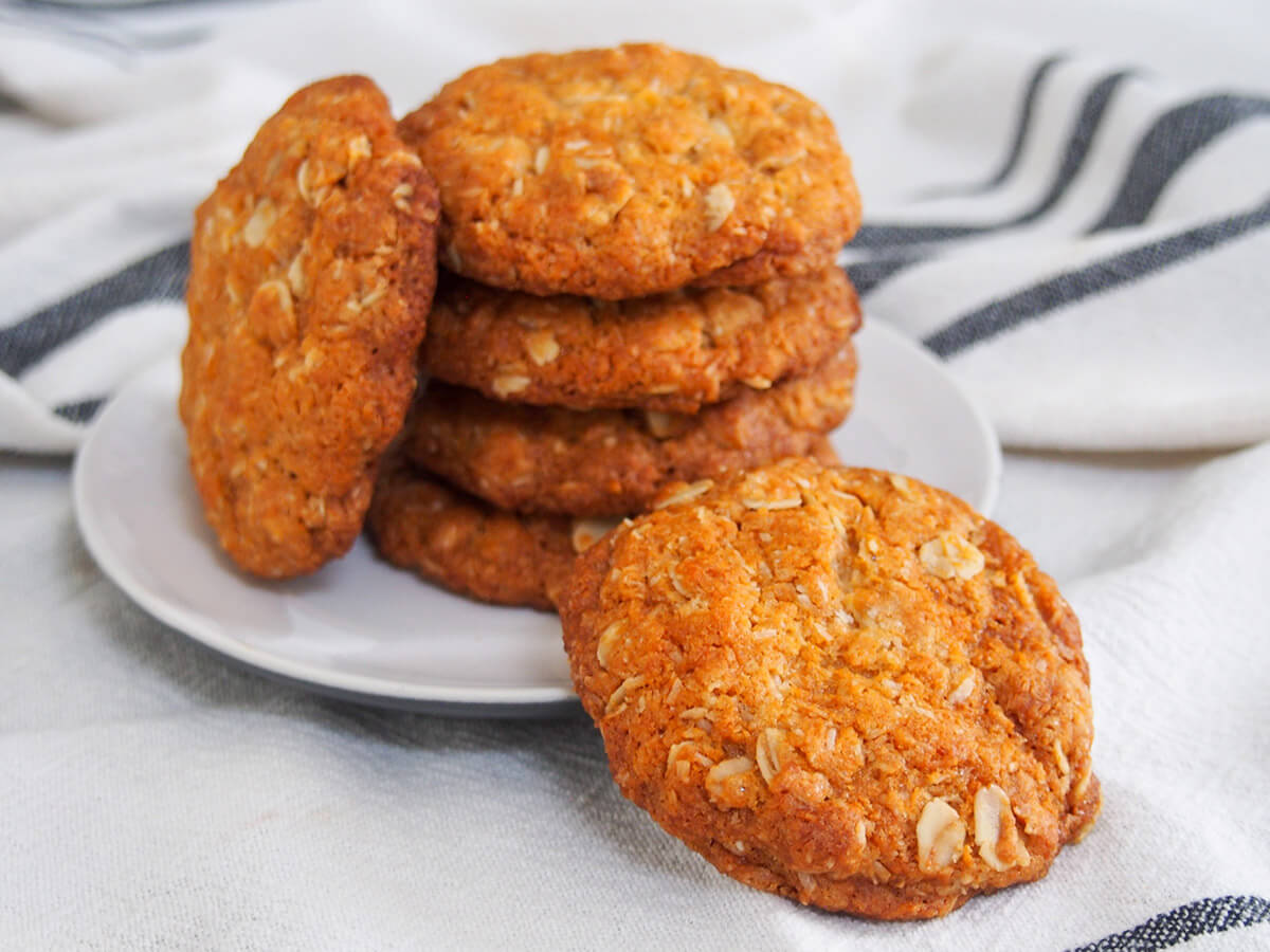 stack of Anzac biscuits with one in front on plate and one rested against stack