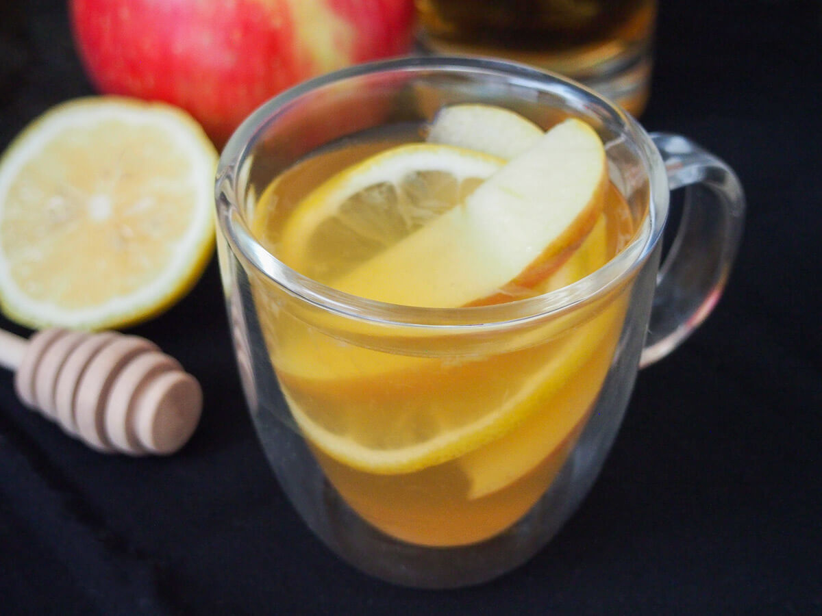 glass of apple brandy hot toddy with cut lemon and honey stirrer to side