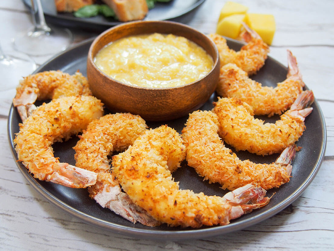 Baked coconut shrimp with mango dipping sauce in bowl at back of plate