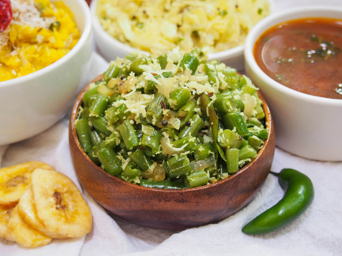 dish of beans thoran with chili to one side and banana chips of other with other dishes behind