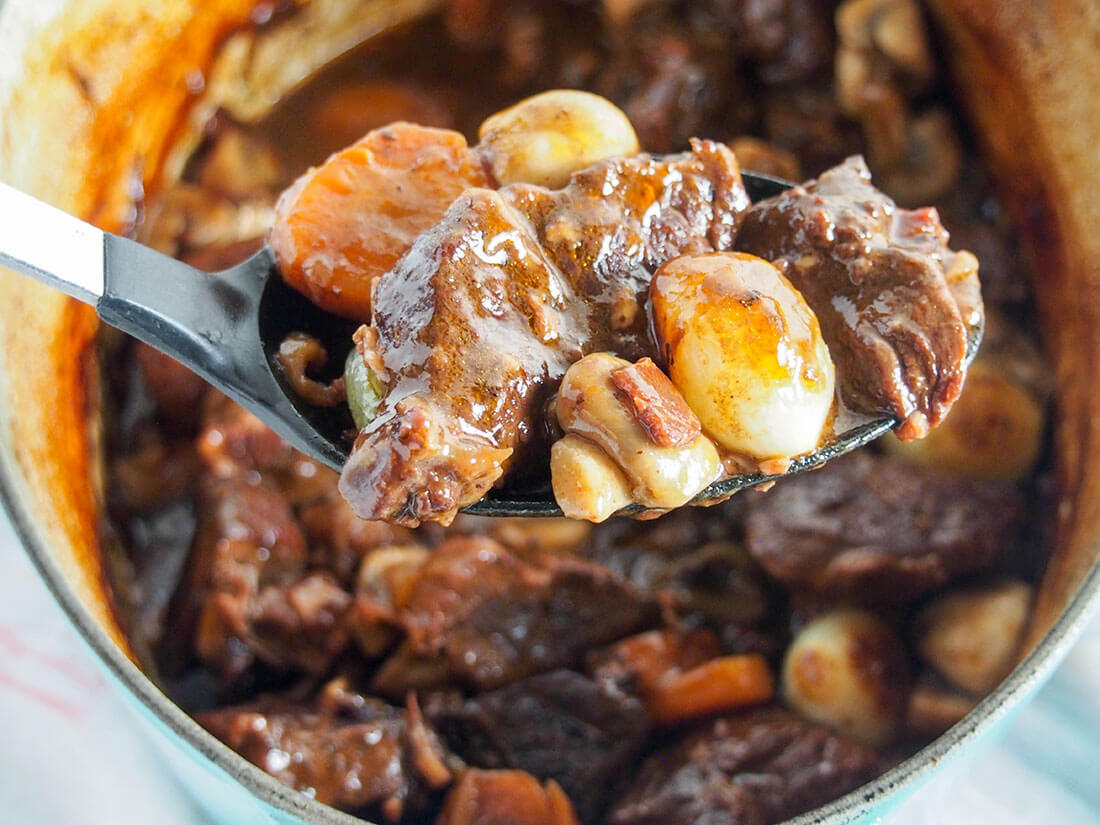 Beef bourguignon with spoonful held in front of pot holding rest