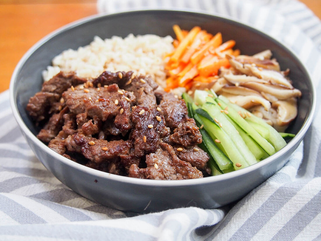 bowl of beef bulgogi with rice and vegetable sides with beef to front of bowl