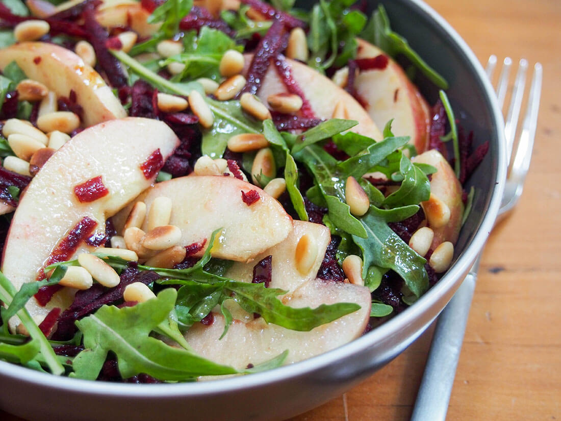 beet apple salad topped with toasted pine nuts with fork to side of bowl