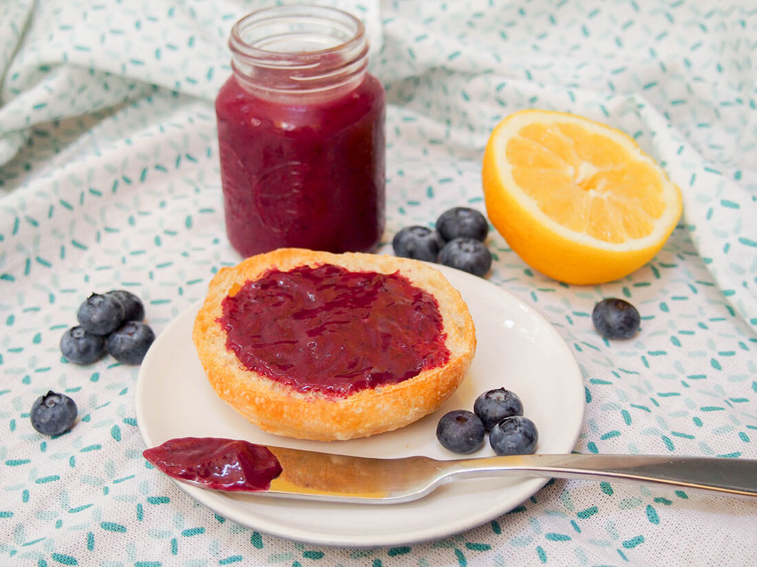 Blueberry curd in jar and on piece of bread with some on knife in front