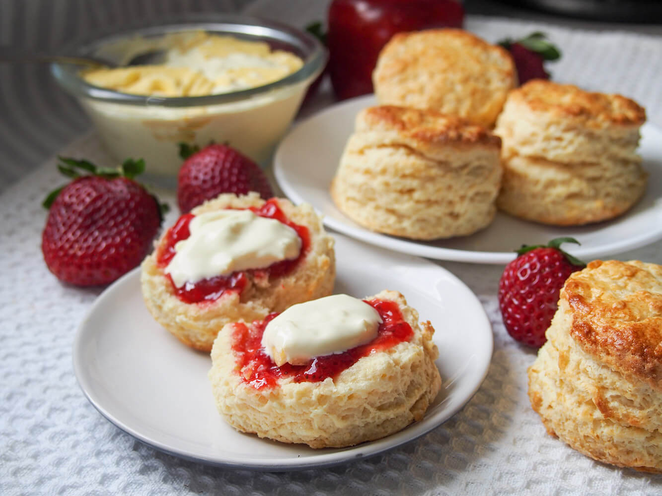 a scone split open and topped with jam and cream with more whole scones on plate behind