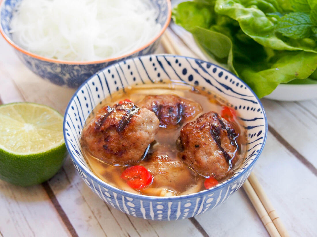 Bun cha Hanoi bowl of meatballs with noodles and salad behind