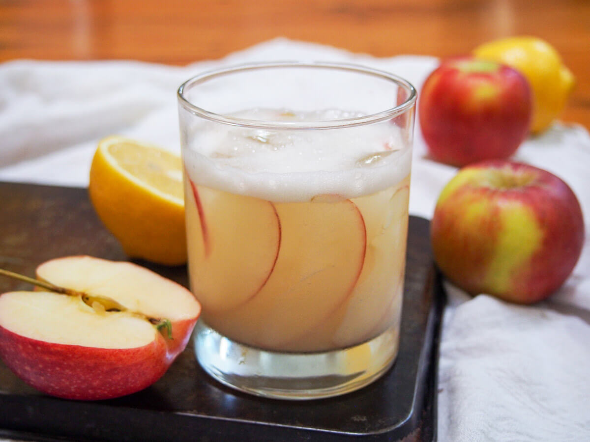 glass of calvados sour with cut apple to side and apples and lemon behind