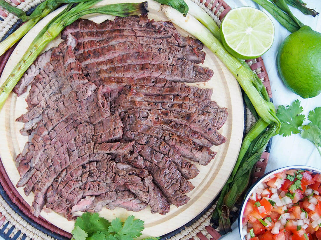 traditional carne asada grilled beef on board with grilled green onions and pico de gallo to side