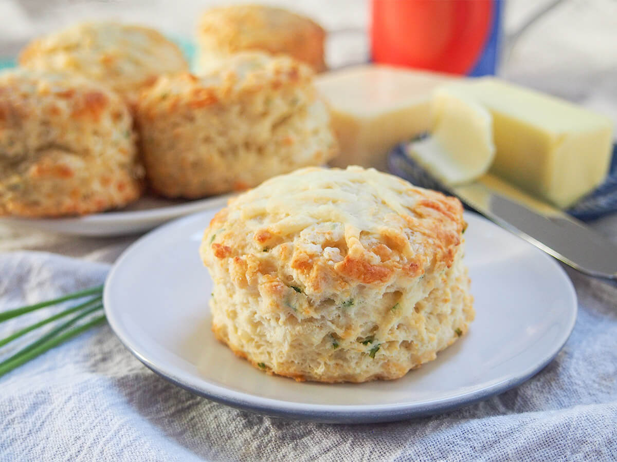 a cheese scone on a small plate with another plate with more behind and fork with butter on it