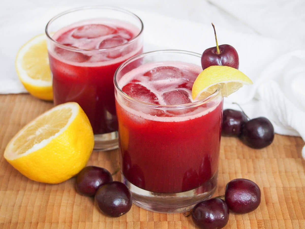 two glasses of cherry lemonade with lemons and cherries to either side