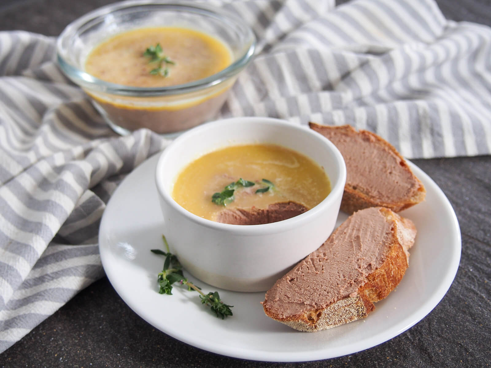 dish of chicken liver pate with some spread on slices of baguette to side and second dish behind