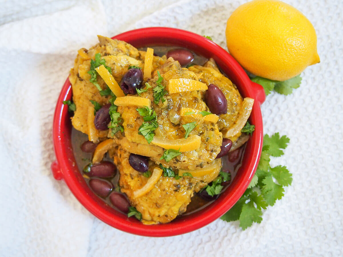 bowl of chicken tagine with preserved lemons and olives from overhead with lemon to side