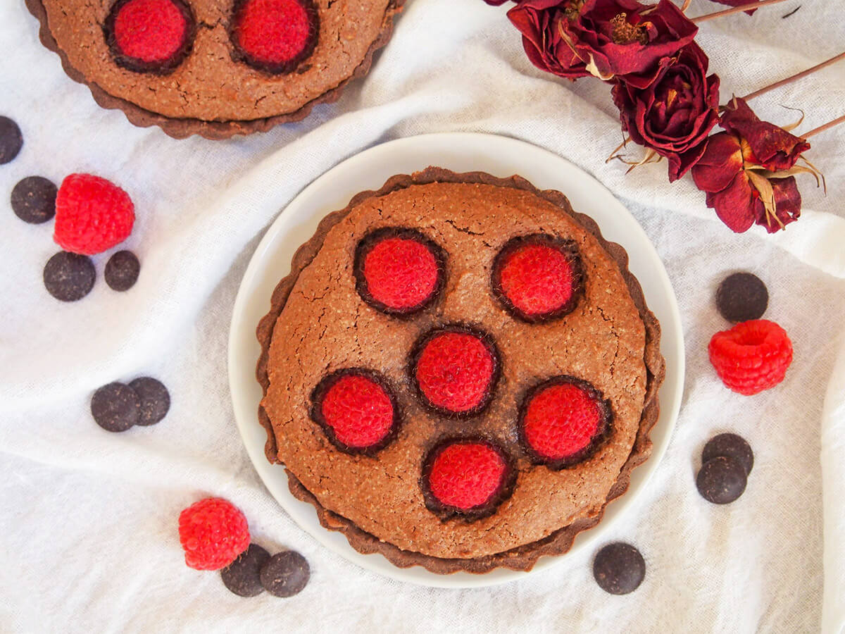 a chocolate almond tart with raspberry with raspberries and chocolate chips around plate