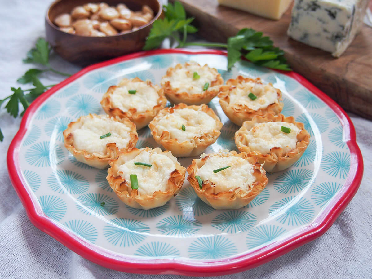 plate of crab phyllo cups with cheeseboard and nuts in part view behind