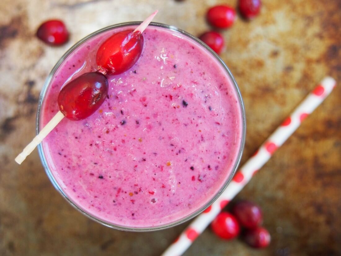 cranberry smoothie viewed from overhead with straw to side and cranberries on top of glass