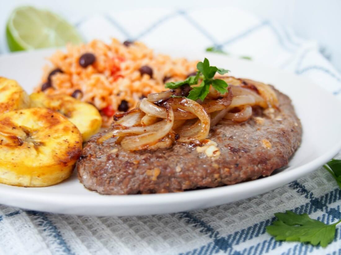 bistec de Palomilla topped with onions with plantain slices to side