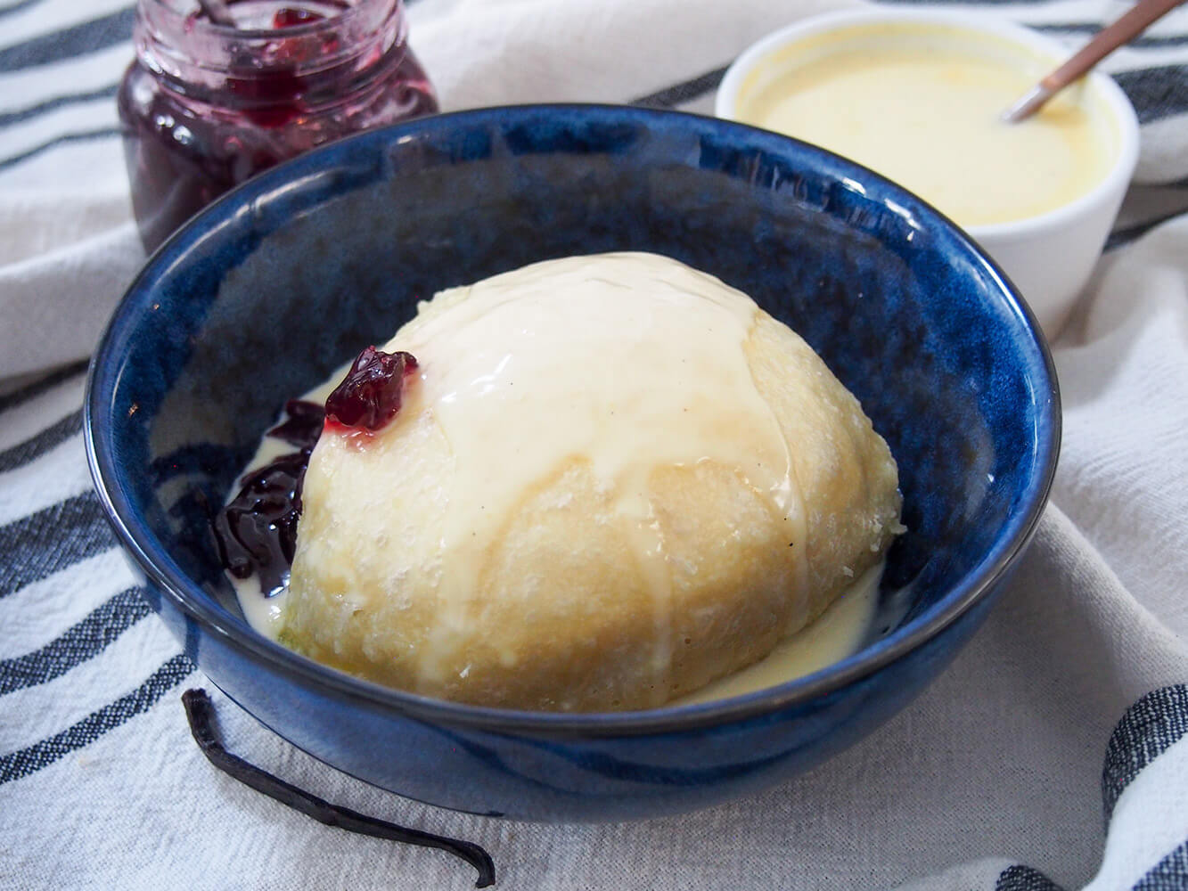 dampfnudel served with vanilla sauce over top and jam to side