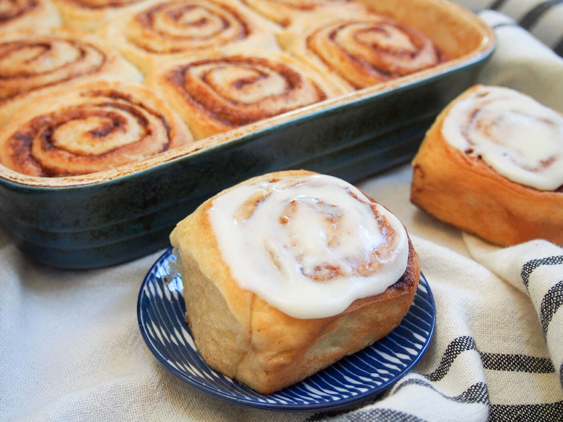 frosted eggnog cinnamon roll on plate in front if dish with more