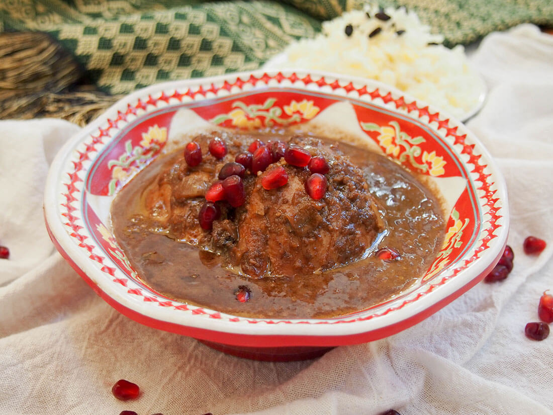 bowl of fesenjan topped with pomegranate arils