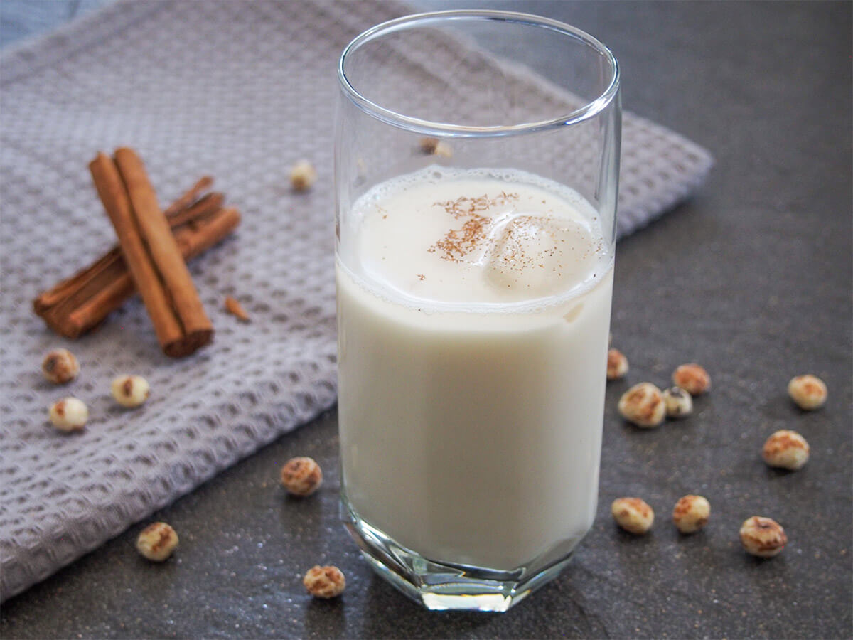 glass of horchata de chufa with tiger nuts and cinnamon sticks behind