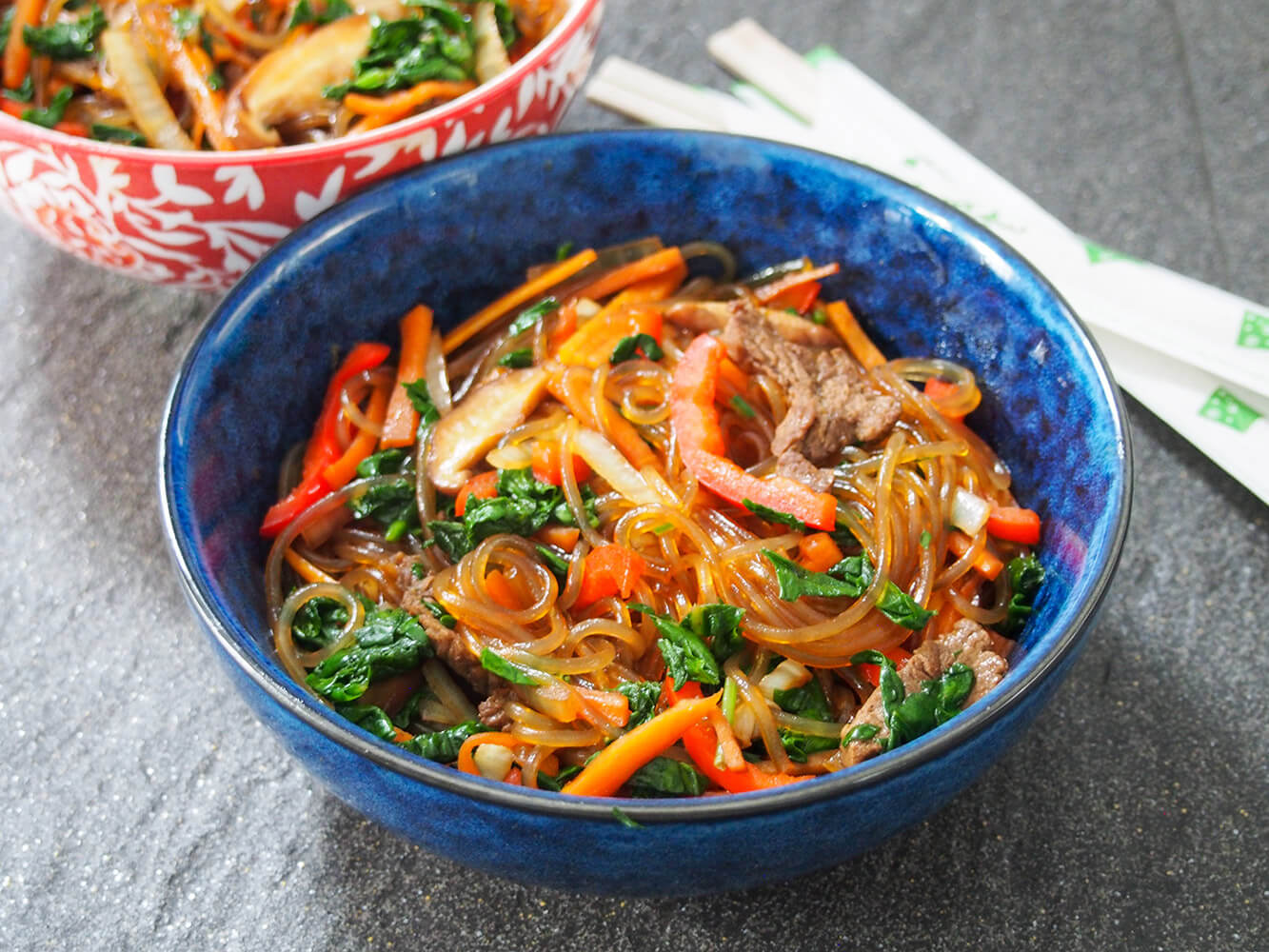 blue bowl filled with japchae (Korean glass noodle stir fry)