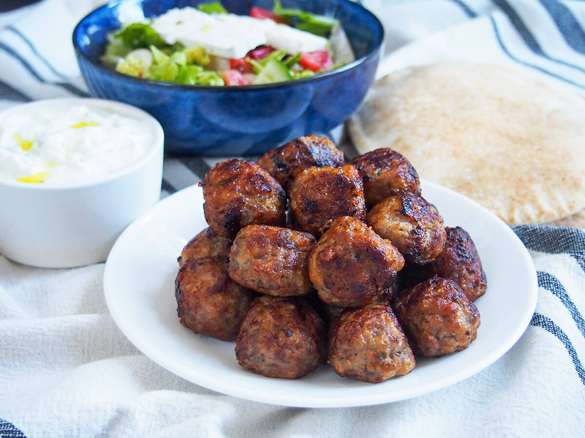 plate of Greek meatballs with tzatziki, salad and pita bread behind