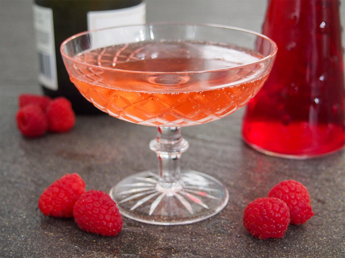 glass of kir imperial raspberry champagne cocktail with bottles behind