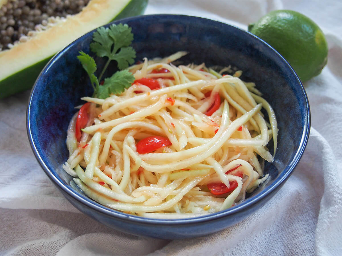 bowl of Lao green papaya salad with lime behind