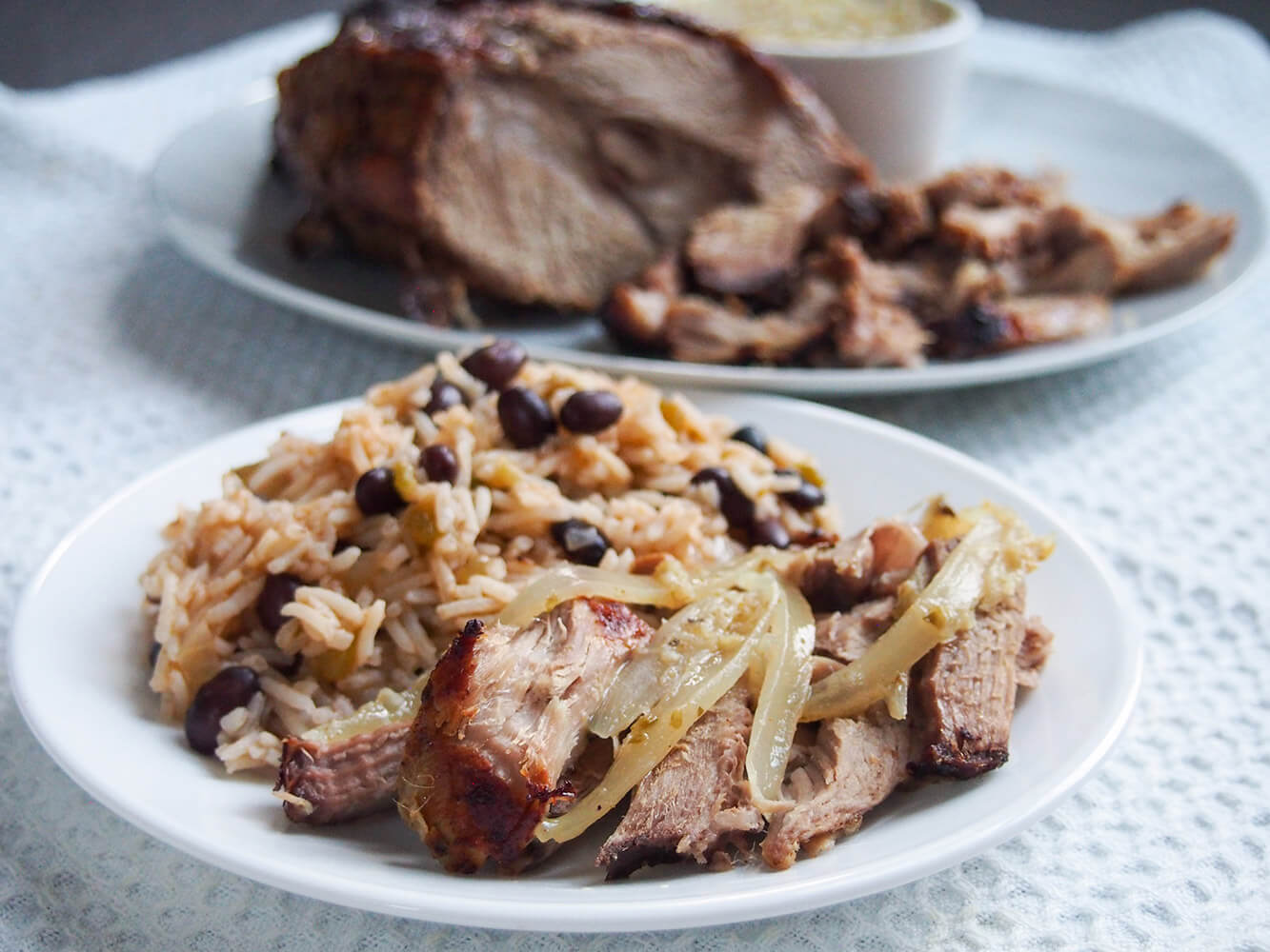 plate with lechon asado topped with mojo sauce and onions, served with rice and black beans