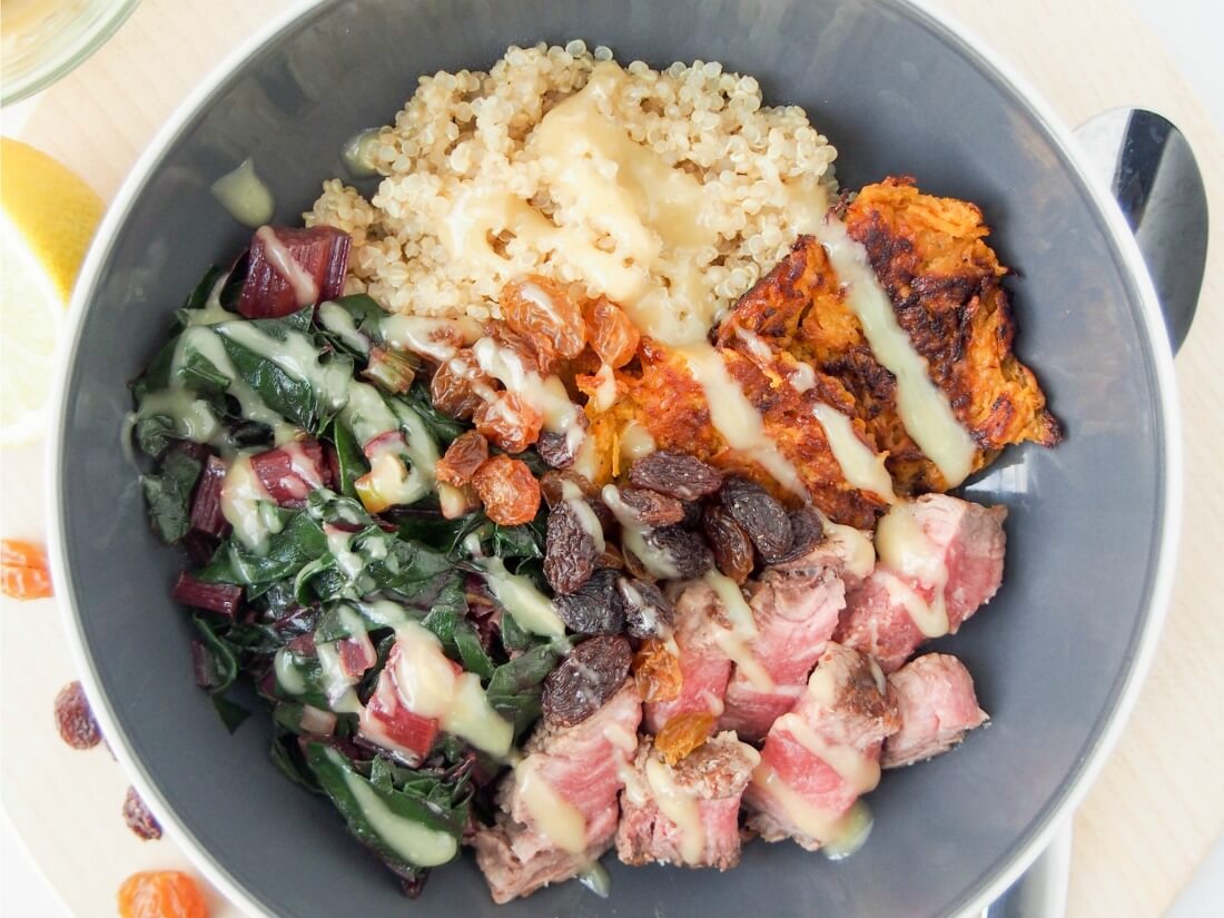 leftover steak and quinoa bowl with dressing drizzled over top and spoon to side of bowl