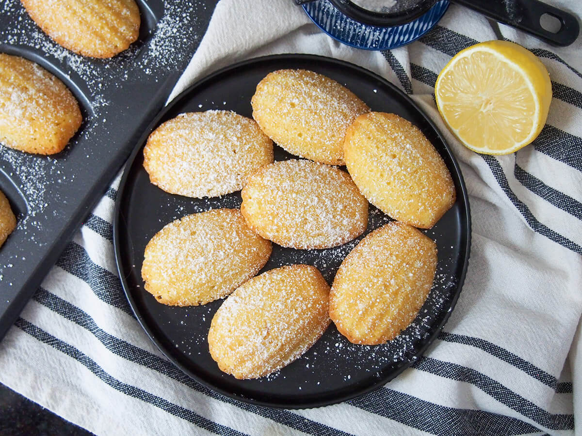 plate of lemon madeleines with half lemon to one side and pan to other