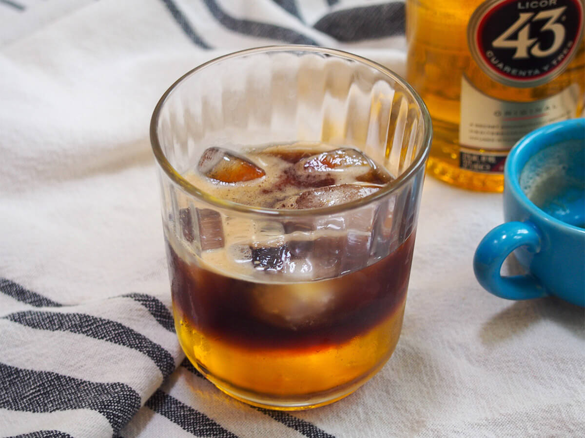 Mexican carajillo coffee cocktail with bottle of licor 43 behind