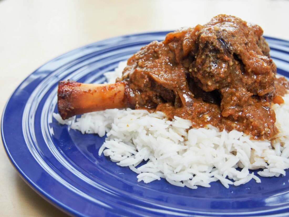 lamb shank with rogan josh sauce over rice on dark blue plate