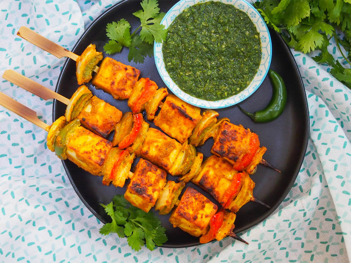 three paneer tikka skewers on plate with green chutney above