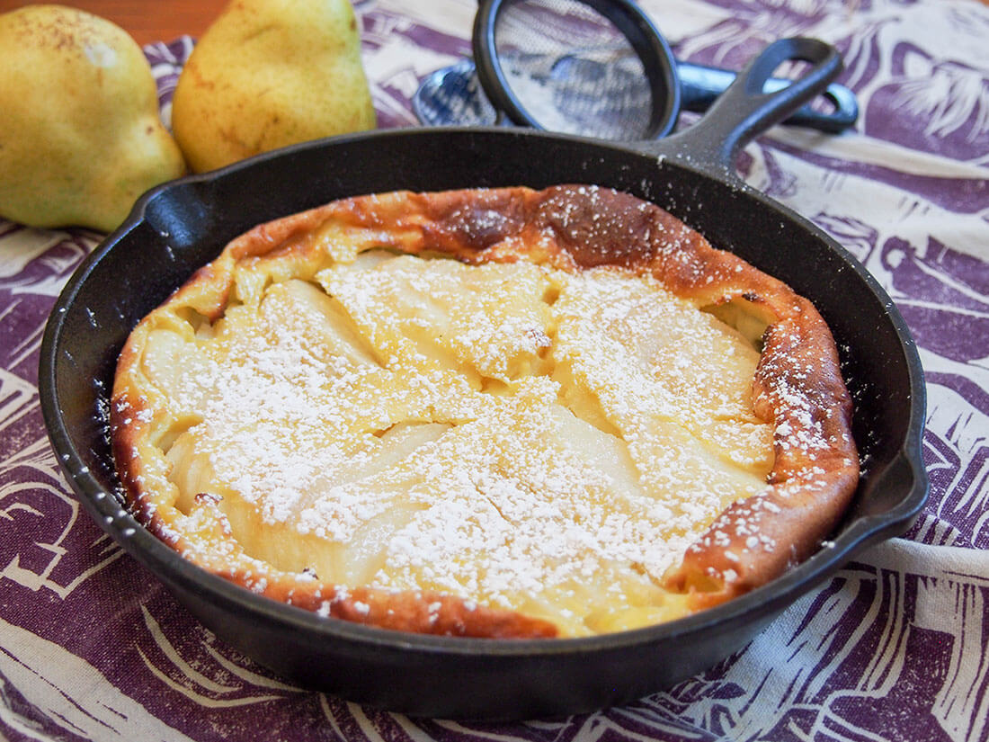 Pear clafoutis in skillet, dusted with sugar, with pears behind