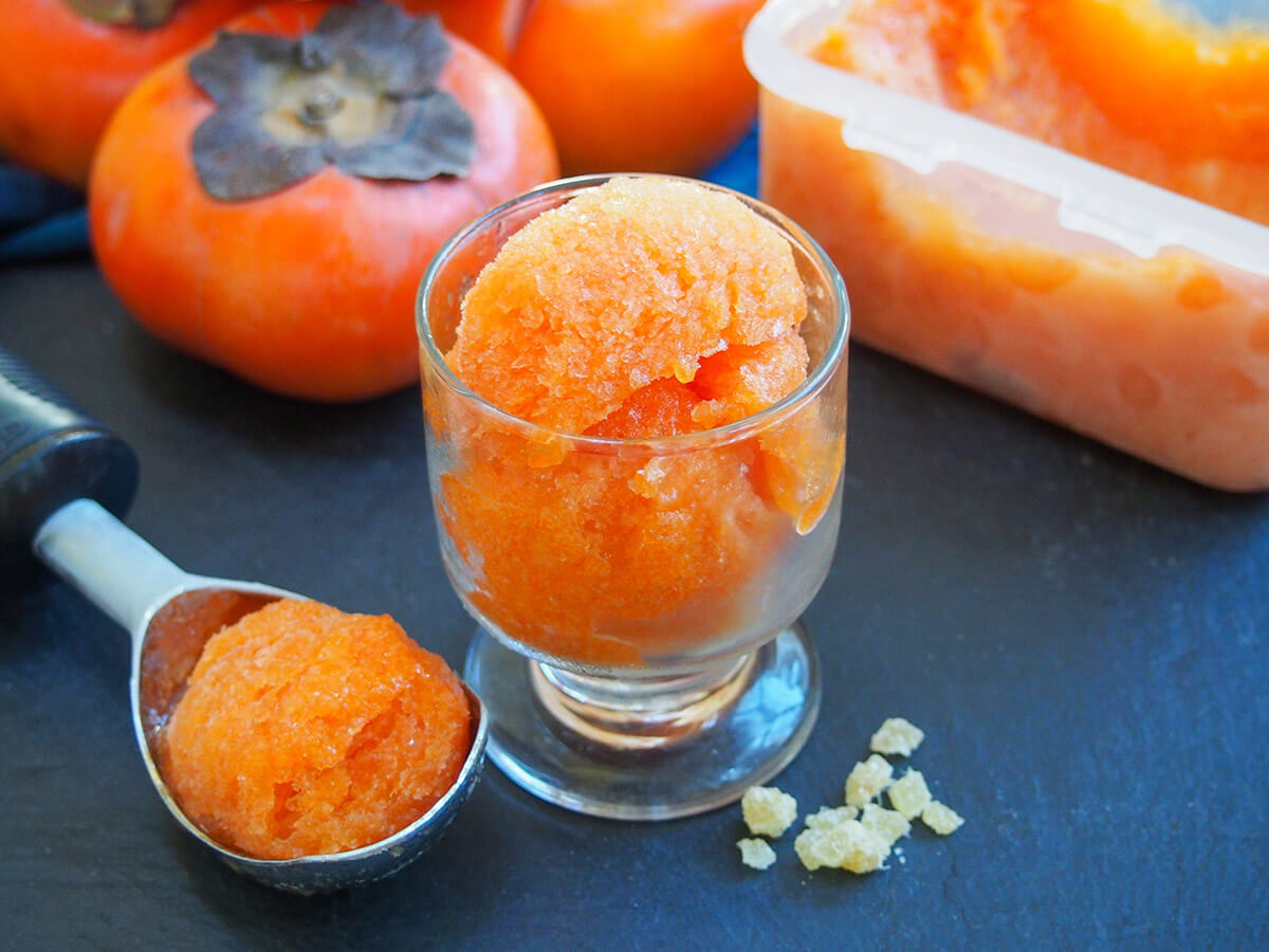 glass with persimmon ginger sorbet with scoop to side and whole fruit behind