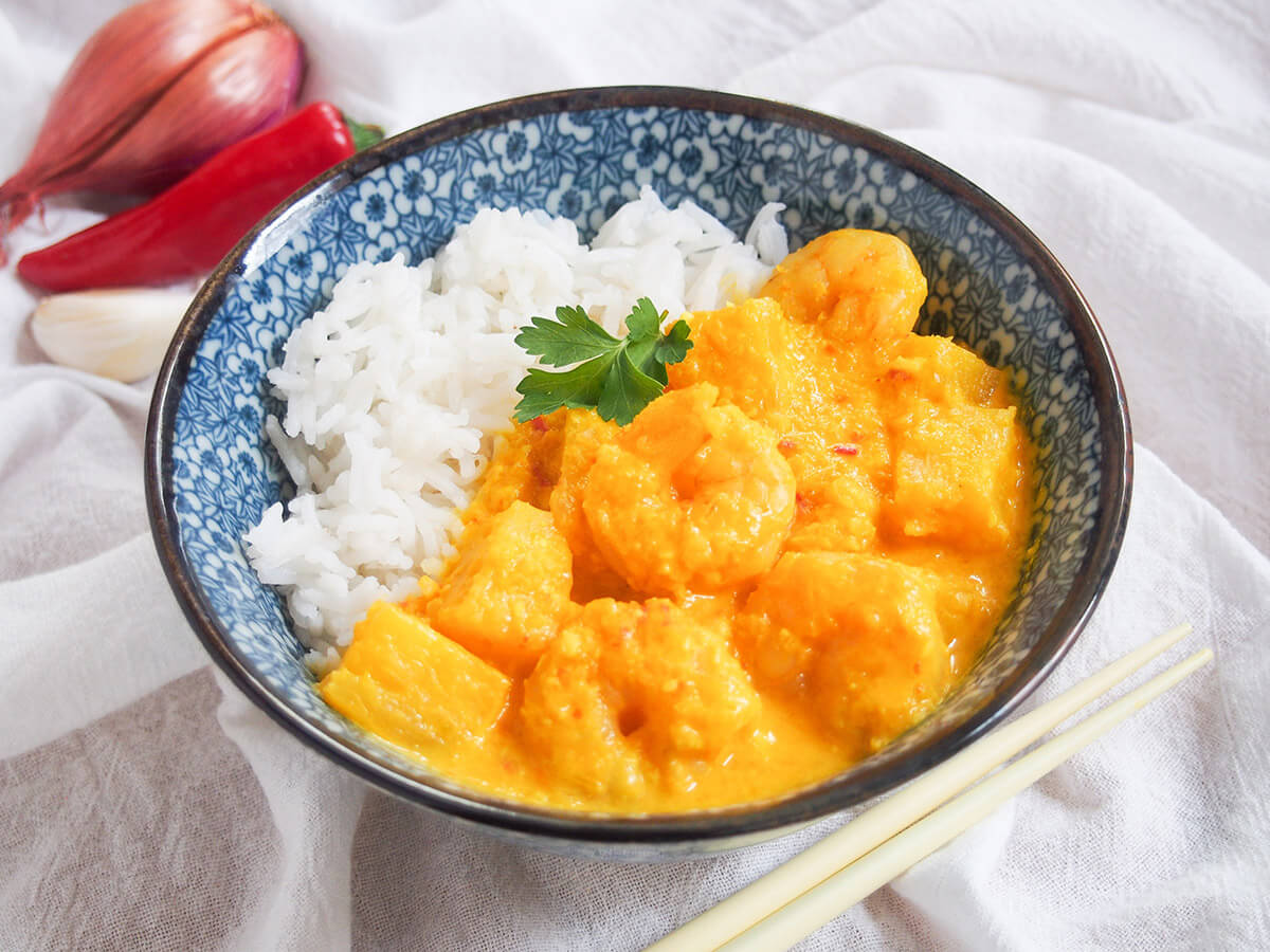 bowl of pineapple shrimp curry with shallot and chili behind