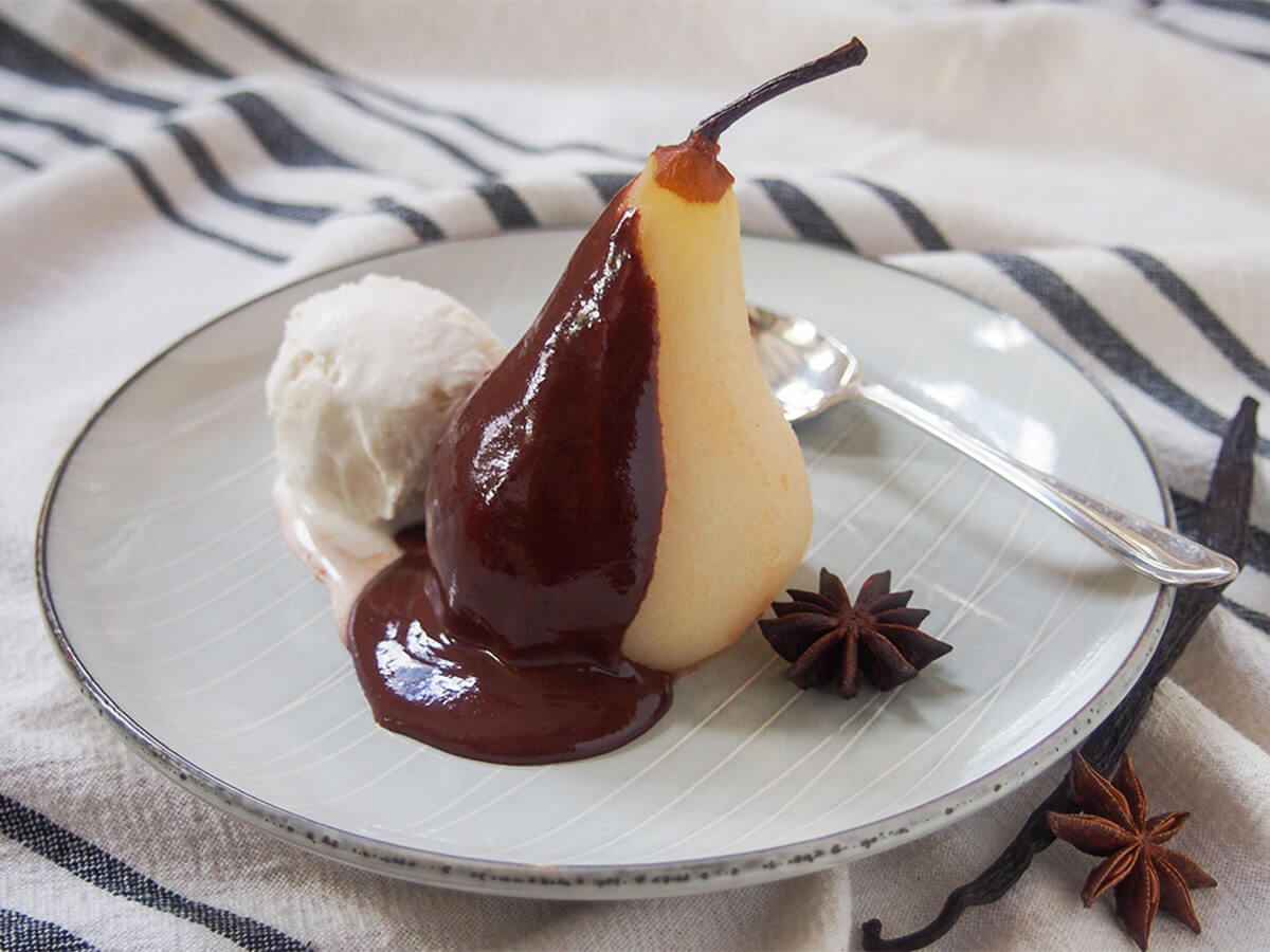 plate of poached pears with chocolate sauce aka poire belle Helene with spoon behind pear