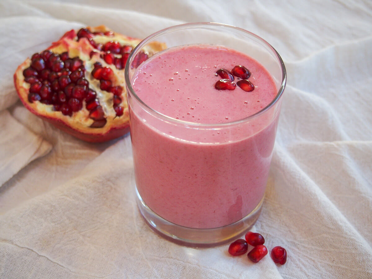 glass of pomegranate smoothie with part of pomegranate behind