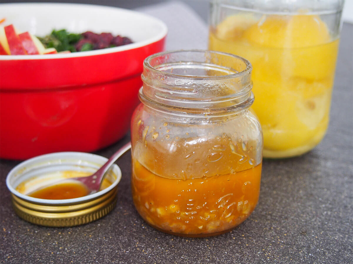 Jar of preserved lemon vinaigrette in front of bowl of salad and jar of preserved lemons