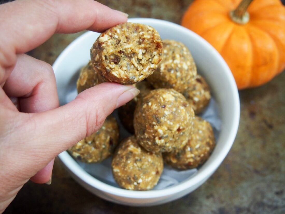 pumpkin energy bite held in hand with bite taken from it and bowl with more behind