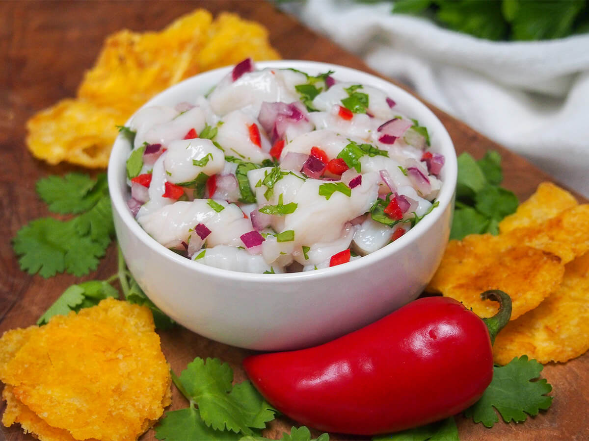 bowl of scallop ceviche with chili in front and plantain chips to side