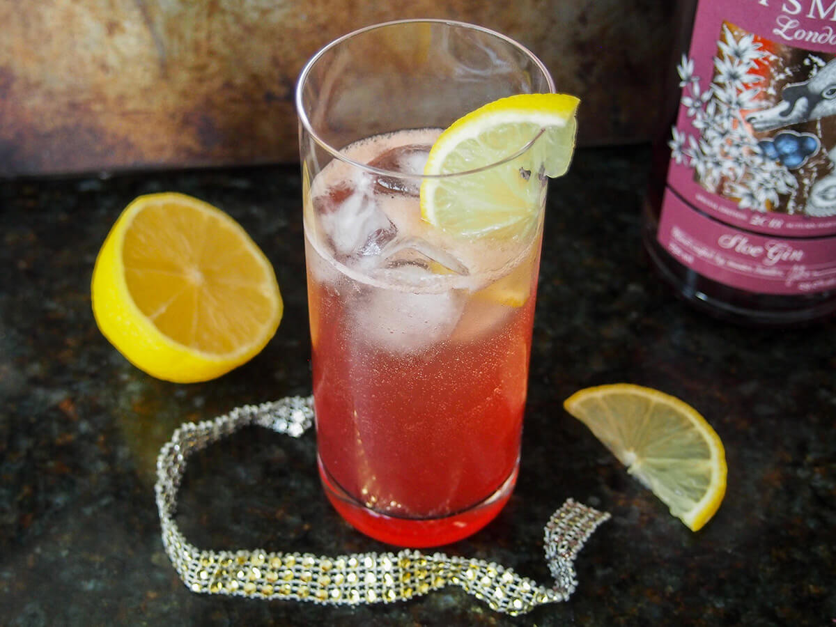 glass of sloe gin fizz with cut lemon to side