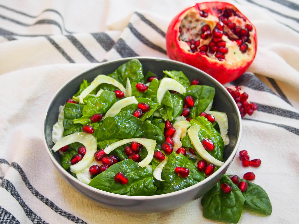 side view of bowl of spinach pomegranate salad with pomegranate behind