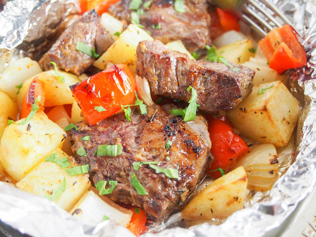 close up view of steak foil packets with potato and pepper