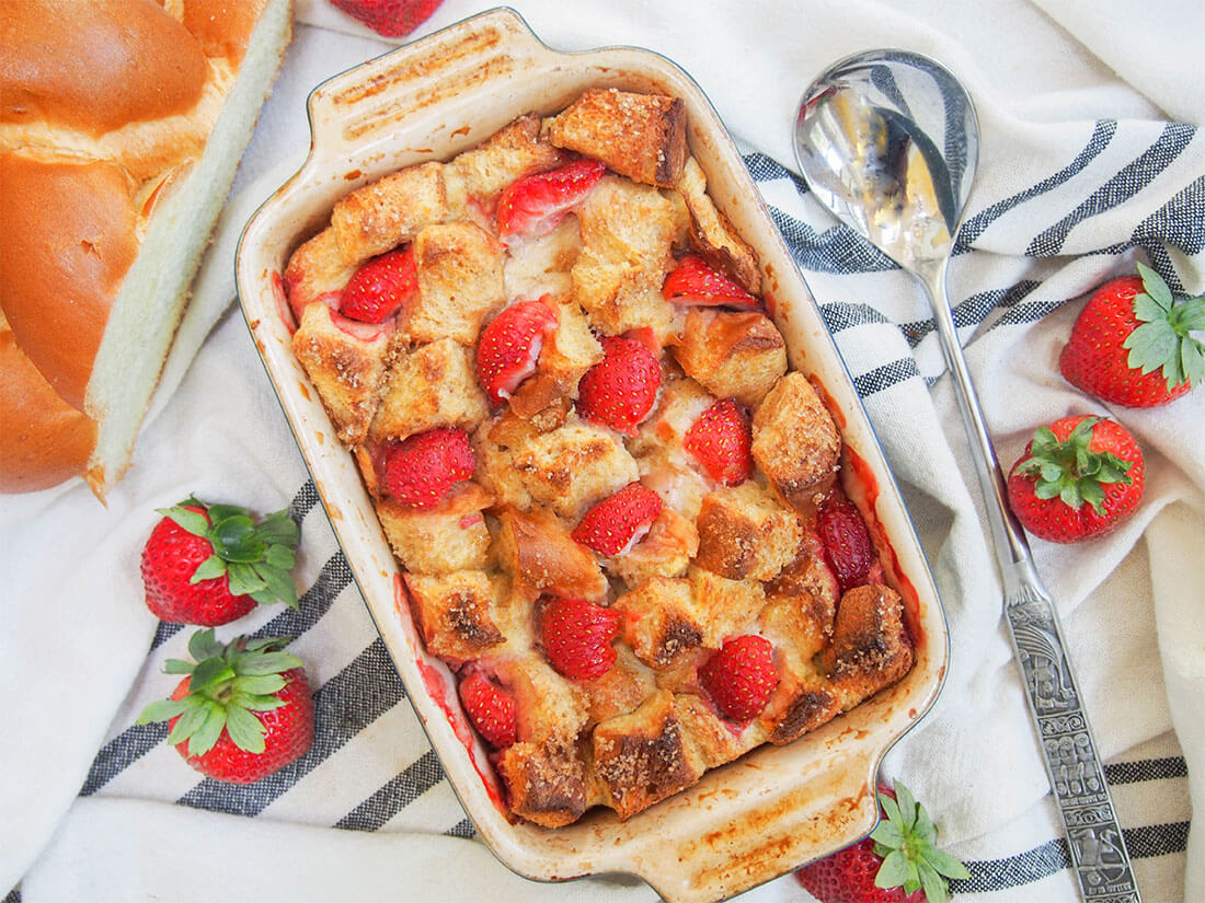 strawberry French toast bake in dish from overhead with spoon to side and strawberries around dish