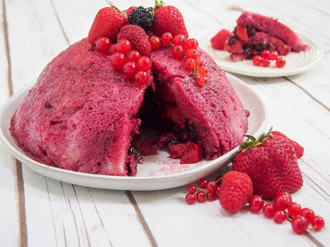 summer pudding on plate with berries to side and slice on plate behind