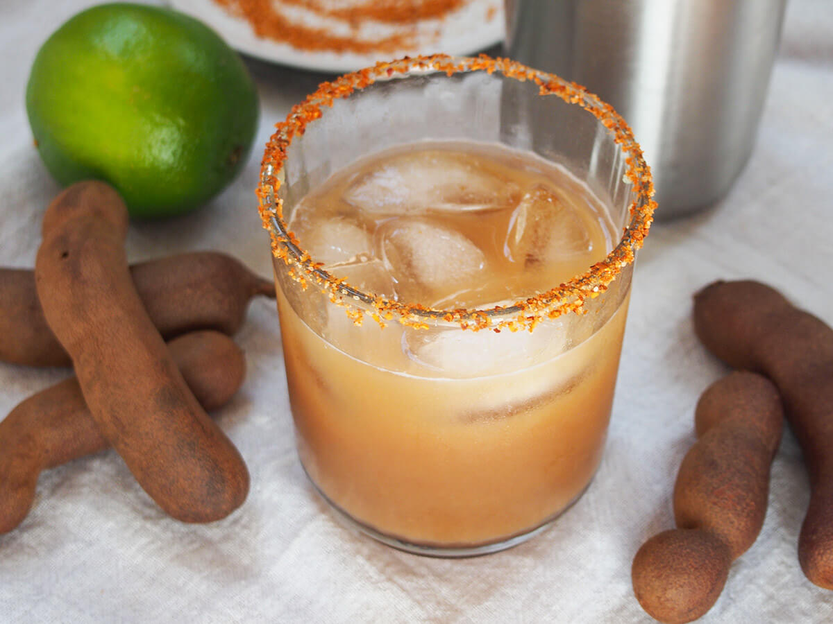 glass of tamarind margarita with tamarind pods either side of glass and lime behind